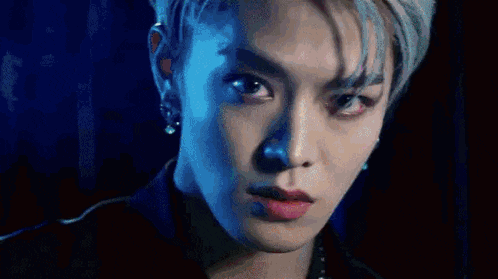 a close up of a young man 's face with a blue background and a piercing in his ear .