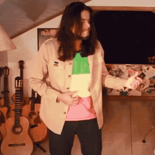 a man with long hair is standing in front of guitars with an iron maiden poster behind him