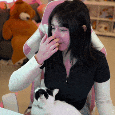 a woman is sitting in a pink chair with a cat on her lap and a teddy bear in the background