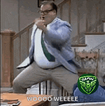 a man in a suit and tie is jumping in the air in a living room while wearing glasses .