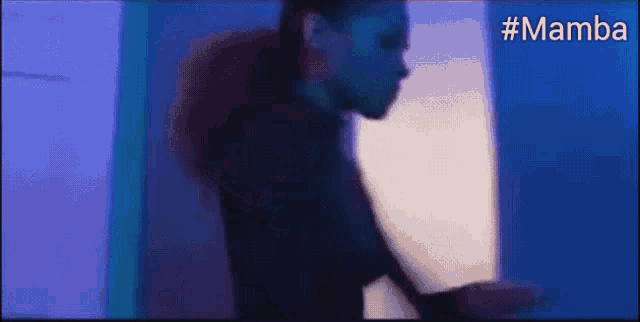 a woman is standing in a dark room with a blue light behind her and the word mamba is on the bottom .
