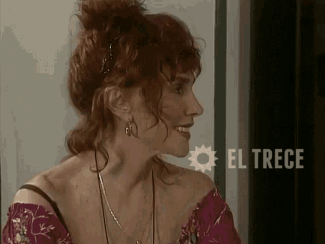 a woman with red hair is smiling in front of an el trece sign