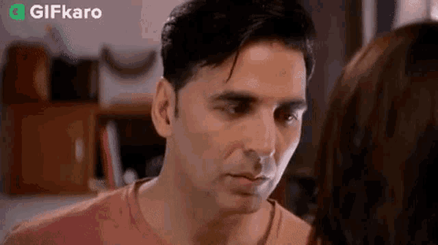 a man and a woman are looking at each other in a room . the man is wearing a pink shirt .