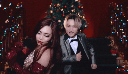 a man in a tuxedo and a woman in a red dress are posing in front of a christmas tree
