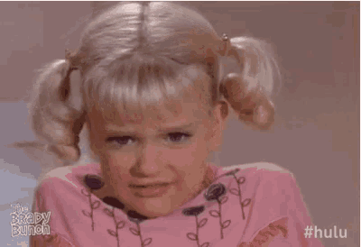 a little girl with pigtails is making a funny face while wearing a pink shirt .