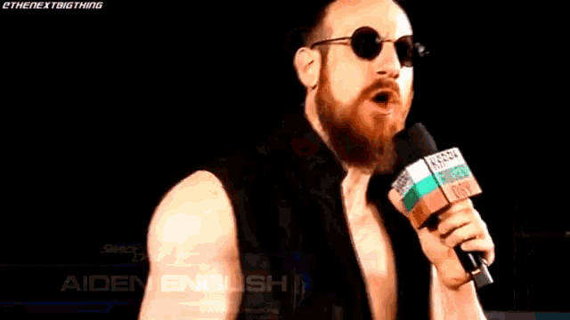 a man with a beard and glasses is holding a microphone with the name aiden english on it
