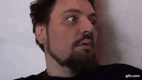 a man with a beard is making a funny face while leaning against a wall .