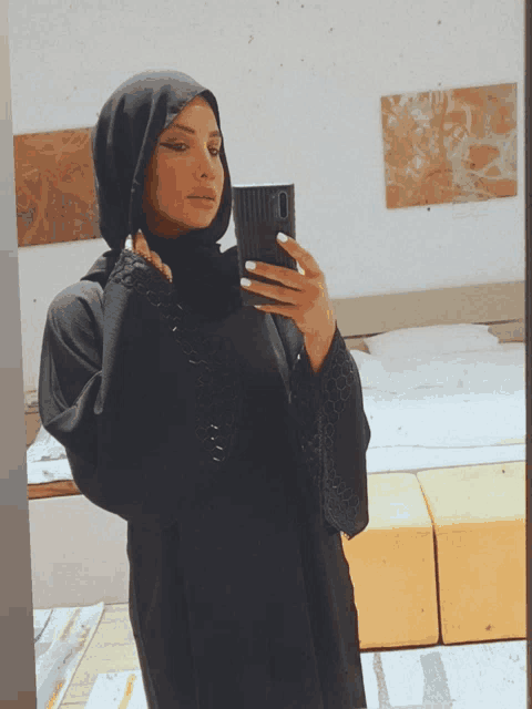 a woman in a hijab takes a selfie with her phone