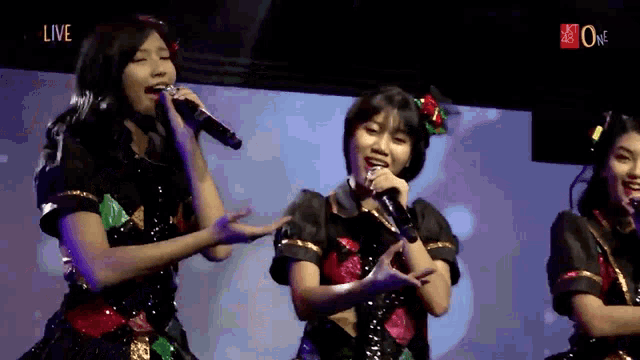a group of girls singing into microphones with the word live in the upper right corner