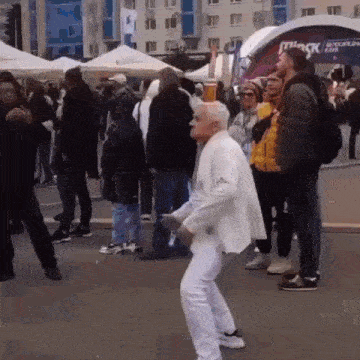 an older man in a white suit is dancing in front of a crowd of people
