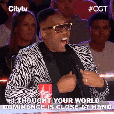 a man in a zebra print suit is speaking into a microphone and says " i thought your world dominance is close at hand
