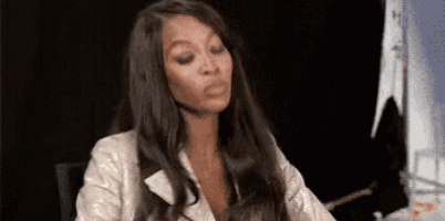 a woman with long hair is sitting at a table and making a face .