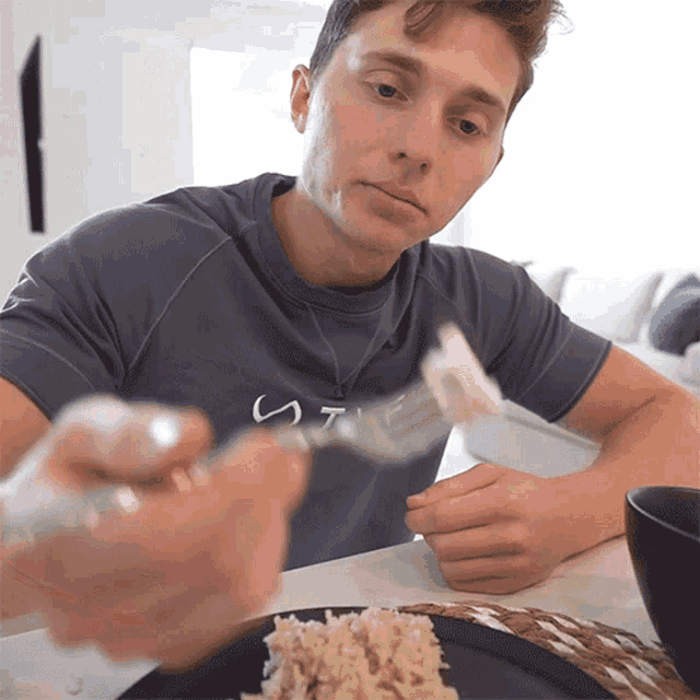 a man sitting at a table with a plate of food and a fork with the letter s on it