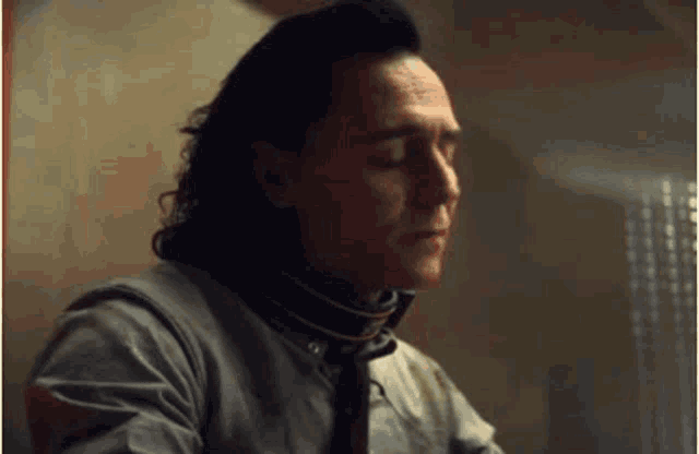a man with long hair is sitting at a table with his eyes closed and a collar around his neck .