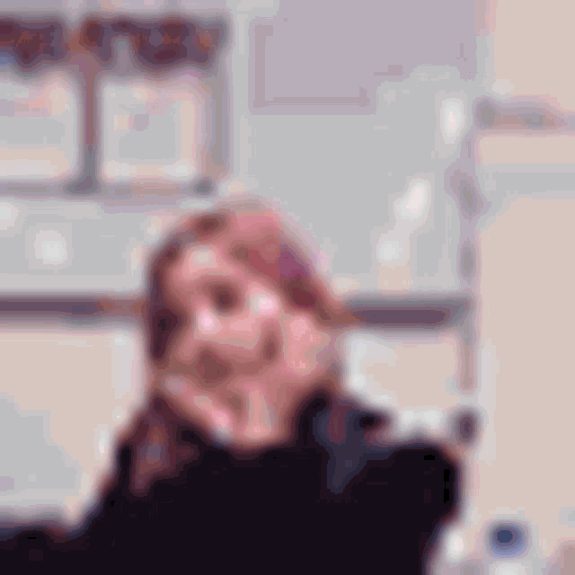 a blurry picture of a woman sitting at a table with her hand on her chin .
