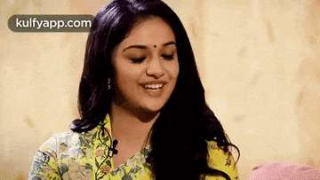 a woman in a yellow shirt is smiling with her eyes closed and a microphone in her mouth .