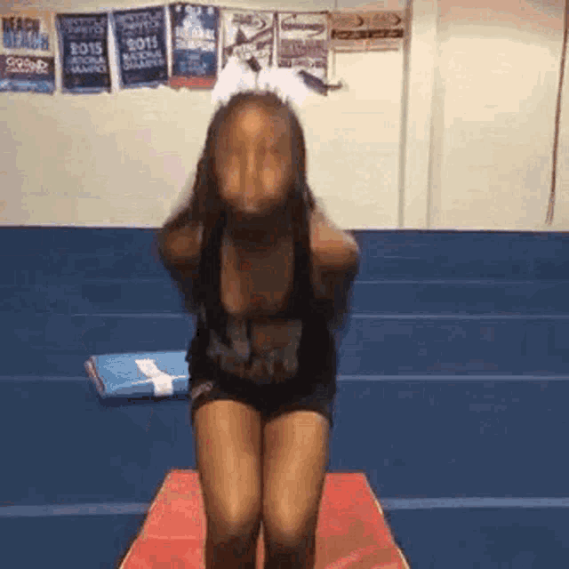 a cheerleader is doing a trick on a mat in a gym while wearing a cheerleading uniform .