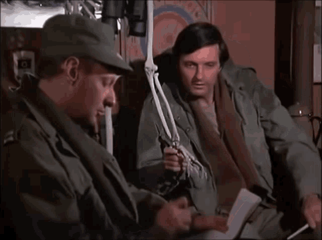 a man in a military uniform is holding a skeleton while another man looks on