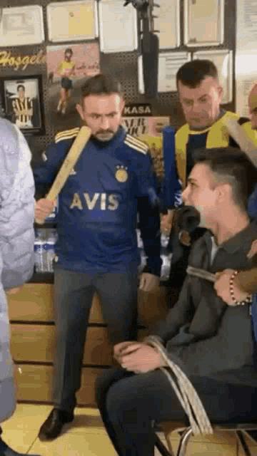 a man wearing a blue avis shirt is holding a baseball bat
