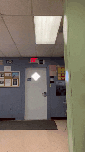 a red exit sign hangs above a white door in a hallway