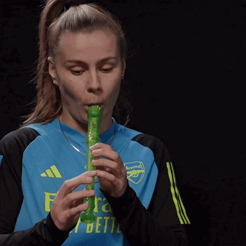 a woman wearing a blue arsenal shirt is playing a green instrument