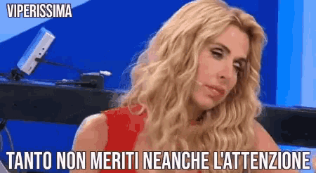 a woman with blonde hair is sitting in front of a blue wall with the words viperissima written above her