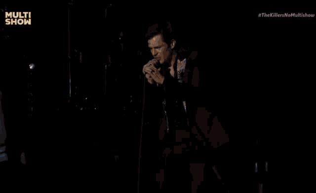 a man in a superman shirt stands in front of a microphone with the words multi show on the bottom right