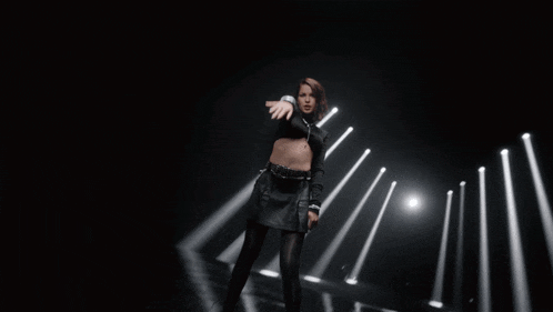 a woman in a black outfit is standing in front of a row of lights