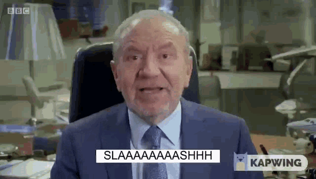 a man in a suit and tie is sitting at a desk and making a funny face .