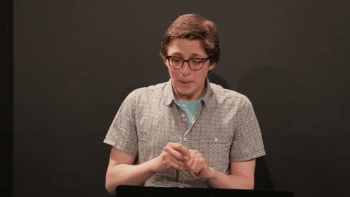 a man wearing glasses and a grey shirt is looking down
