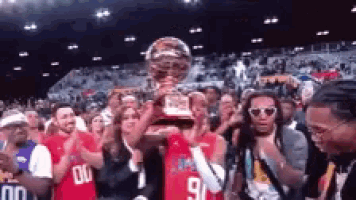 a basketball player is holding up a trophy in front of a crowd of people .
