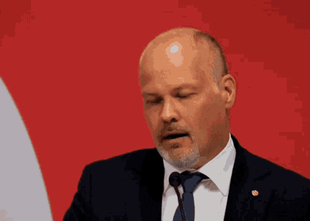a man in a suit and tie is speaking into a microphone with his eyes closed