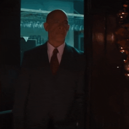 a bald man in a suit and tie holds his hand to his mouth