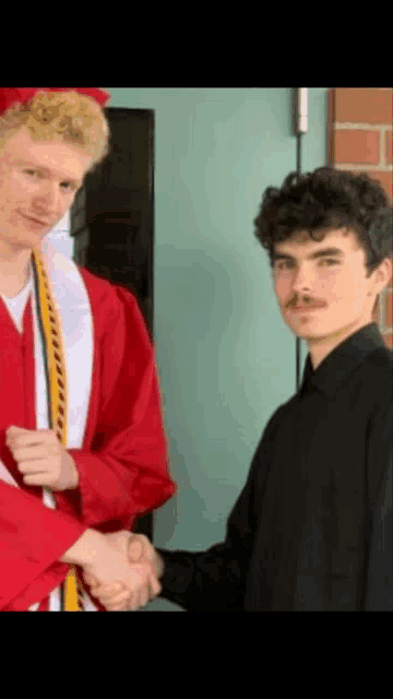 a man in a graduation cap and gown shakes hands with another man