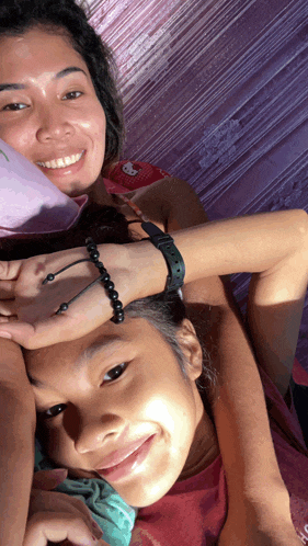 a woman wearing a hello kitty hat is laying next to a girl with a bracelet on her wrist