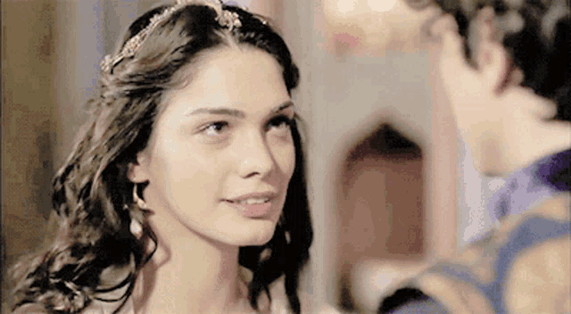a woman wearing a tiara and earrings looks at a man