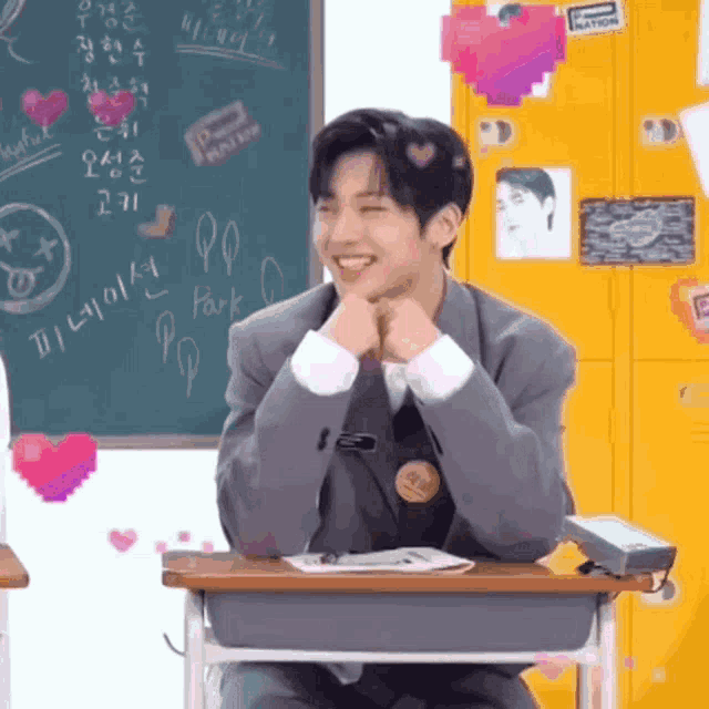 a young man in a suit sits at a desk in front of a blackboard that says park