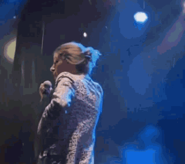 a woman is singing into a microphone with her arm in the air