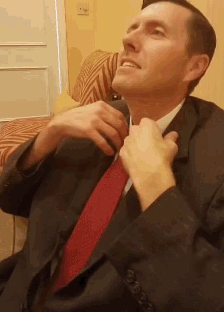 a man in a suit adjusts his red tie