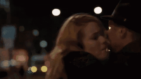 a man and a woman are kissing in a dark room . the woman is wearing a hat .