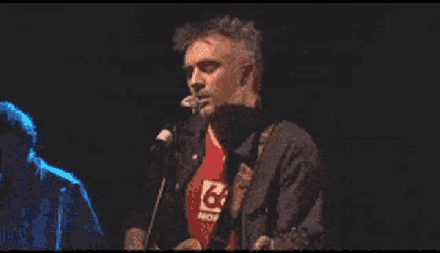 a man singing into a microphone wearing a red shirt that says g on it