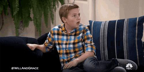 a young boy in a plaid shirt is sitting on a couch with a surprised look on his face .