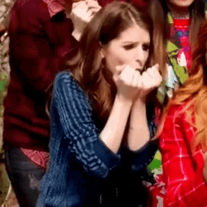 a woman is covering her mouth with her hands while standing in a crowd of people .