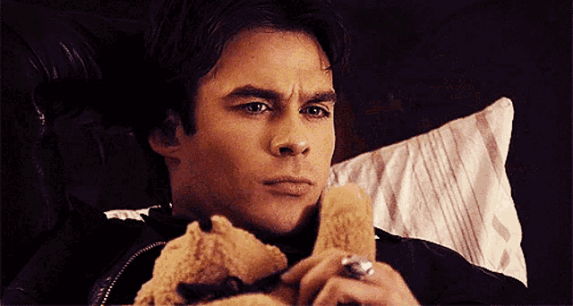 a man laying in bed holding a teddy bear