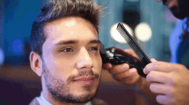 a man getting his hair cut by a barber with a comb