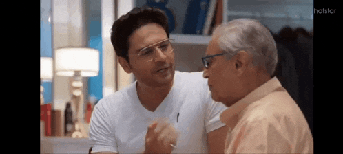 a man wearing glasses is talking to an older man in a room .