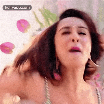 a close up of a woman 's face with her hair blowing in the wind and flowers in the background .