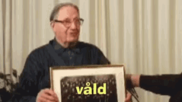 an older man is holding a framed picture with the word vald on it .