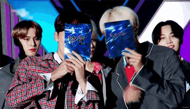 a group of young men are standing next to each other and one of them is holding a blue bag that says mnet on it