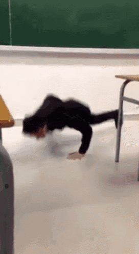 a person is doing push ups on the floor in a classroom in front of a green board .